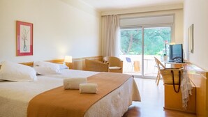 A hotel room with two beds, a desk with a computer, a chair, and a large window with a view of trees. - Hotel Ancora (Palamós)
