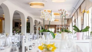 A restaurant interior with white tables, orchid plants, and hanging pendant lights. - Hotel Ancora (Palamós)