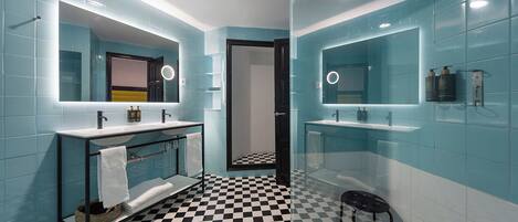 Un baño con dos lavamanos, un espejo, piso a cuadros blanco y negro y paredes con azulejos azules.