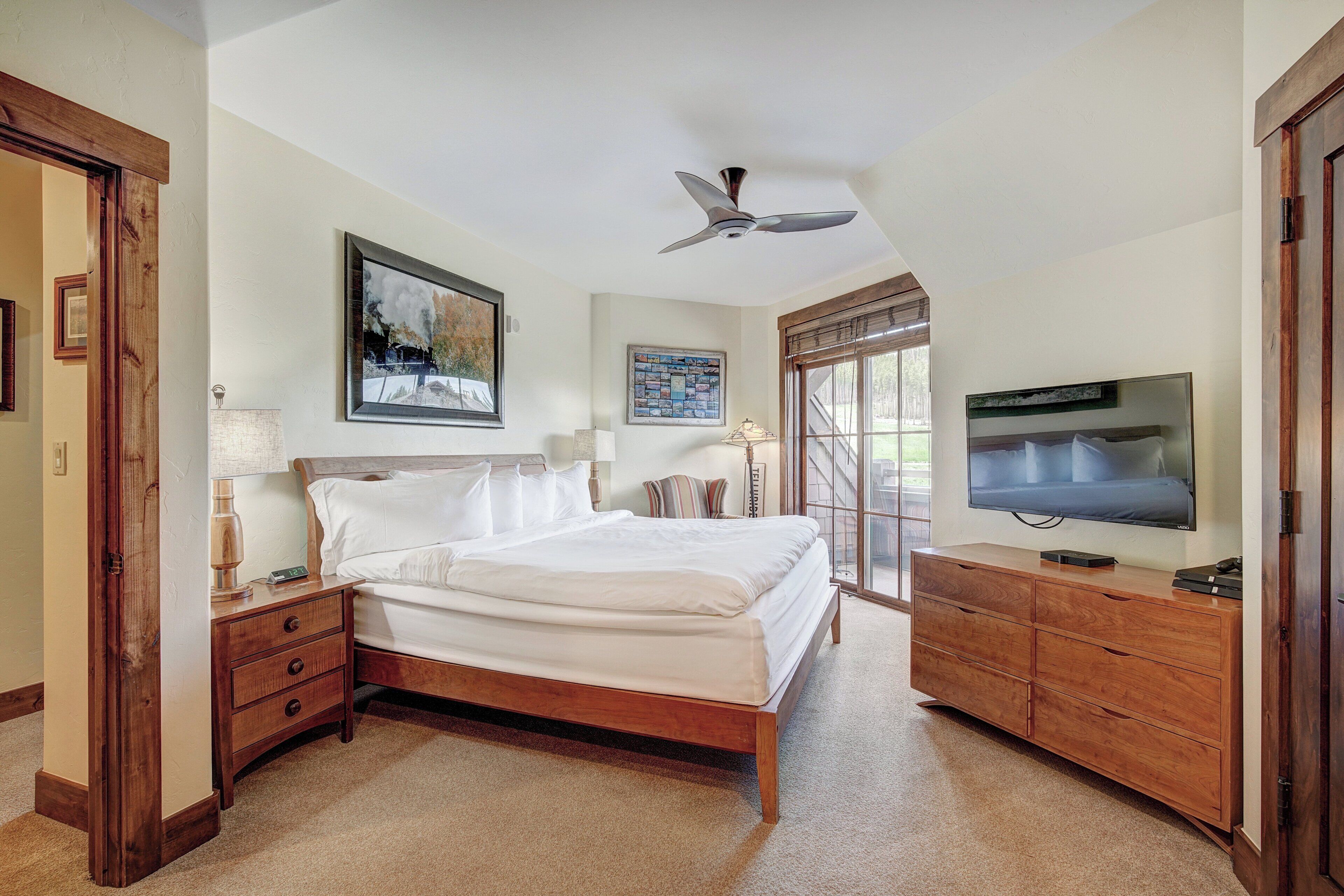 Quarto com cama, mesas de cabeceira, cômoda, ventilador de teto e televisão.