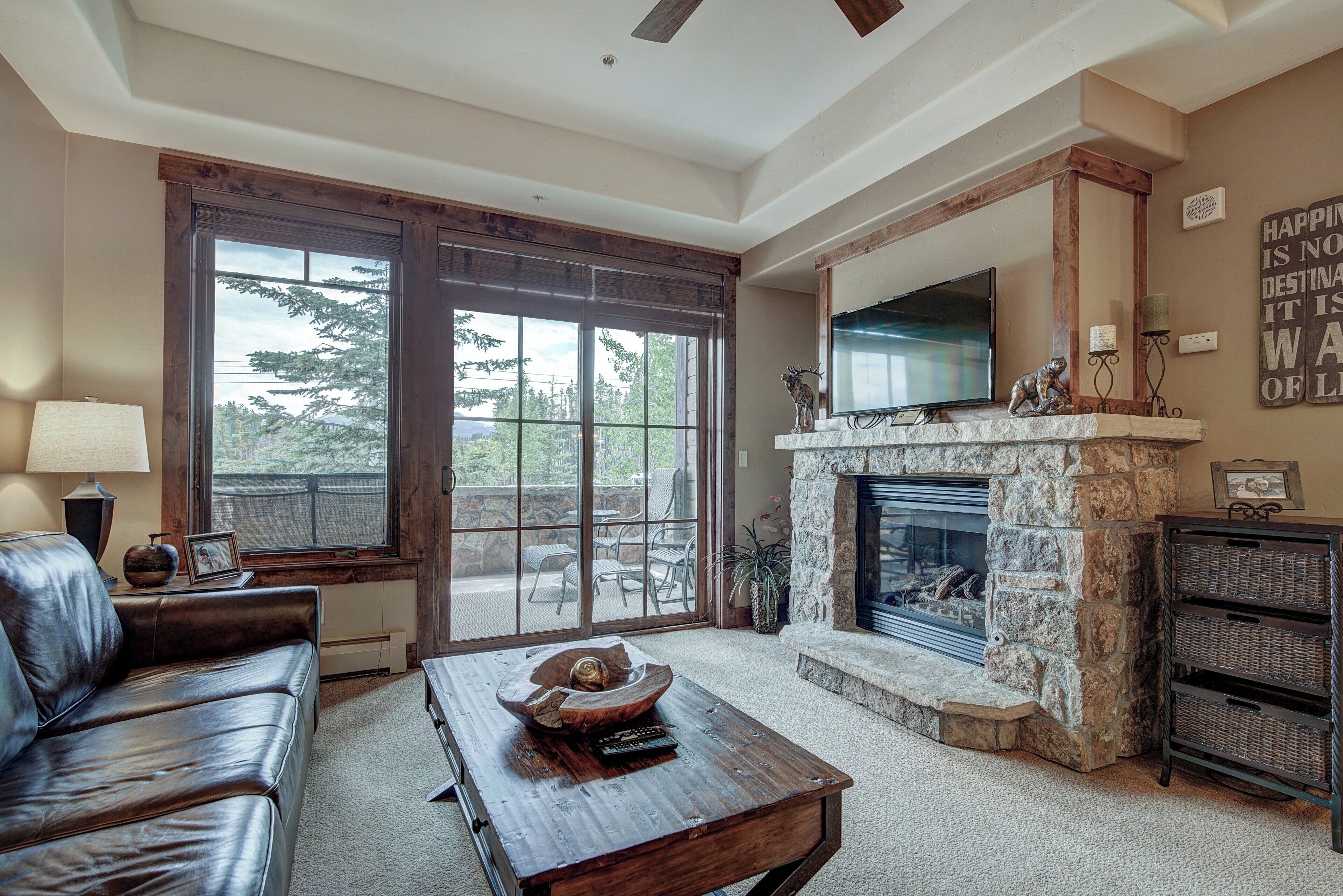 A living room with a stone fireplace, leather sofa, and a television mounted above it.