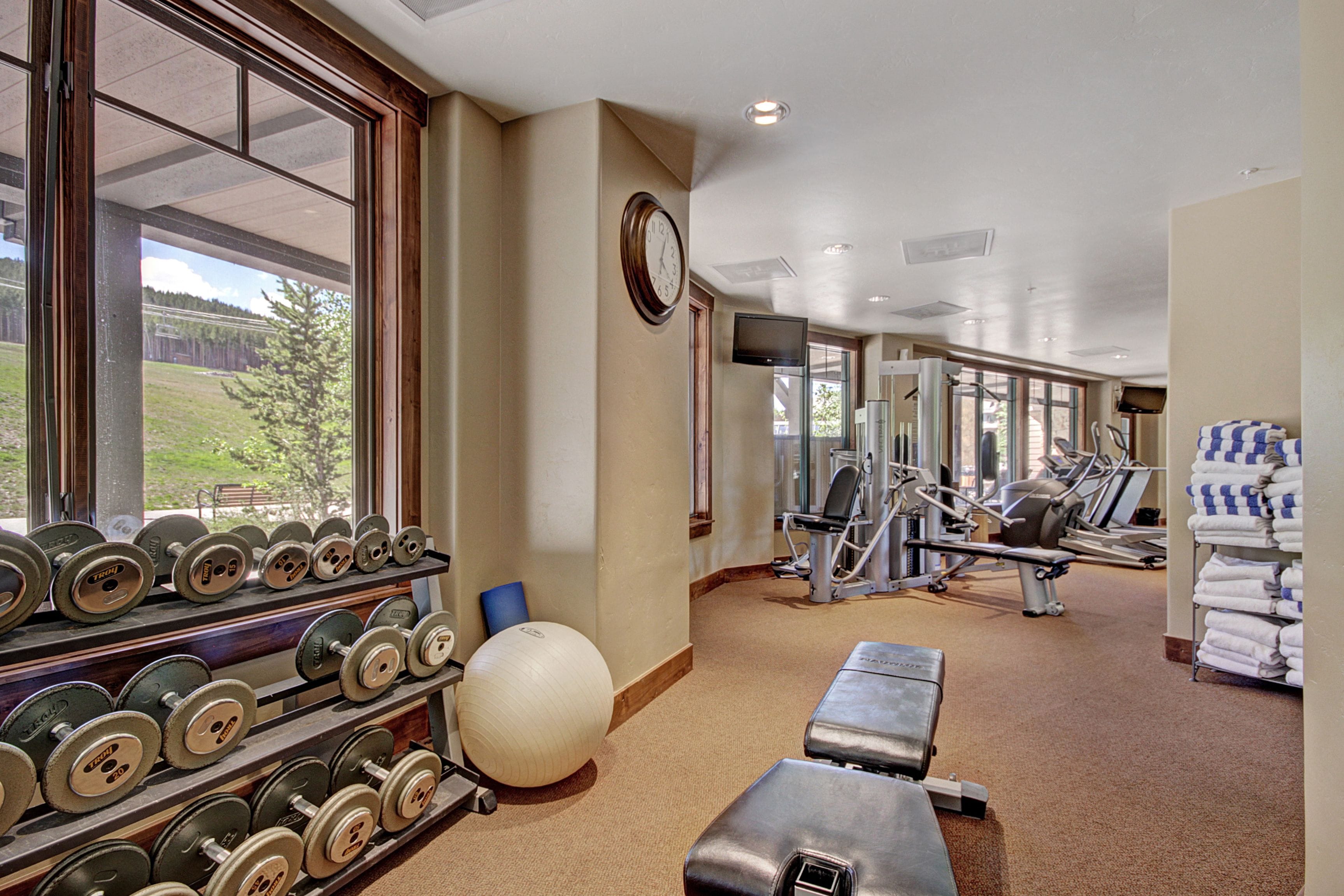 Ein Fitnessraum mit Trainingsgeräten, einer Uhr und Blick ins Freie.