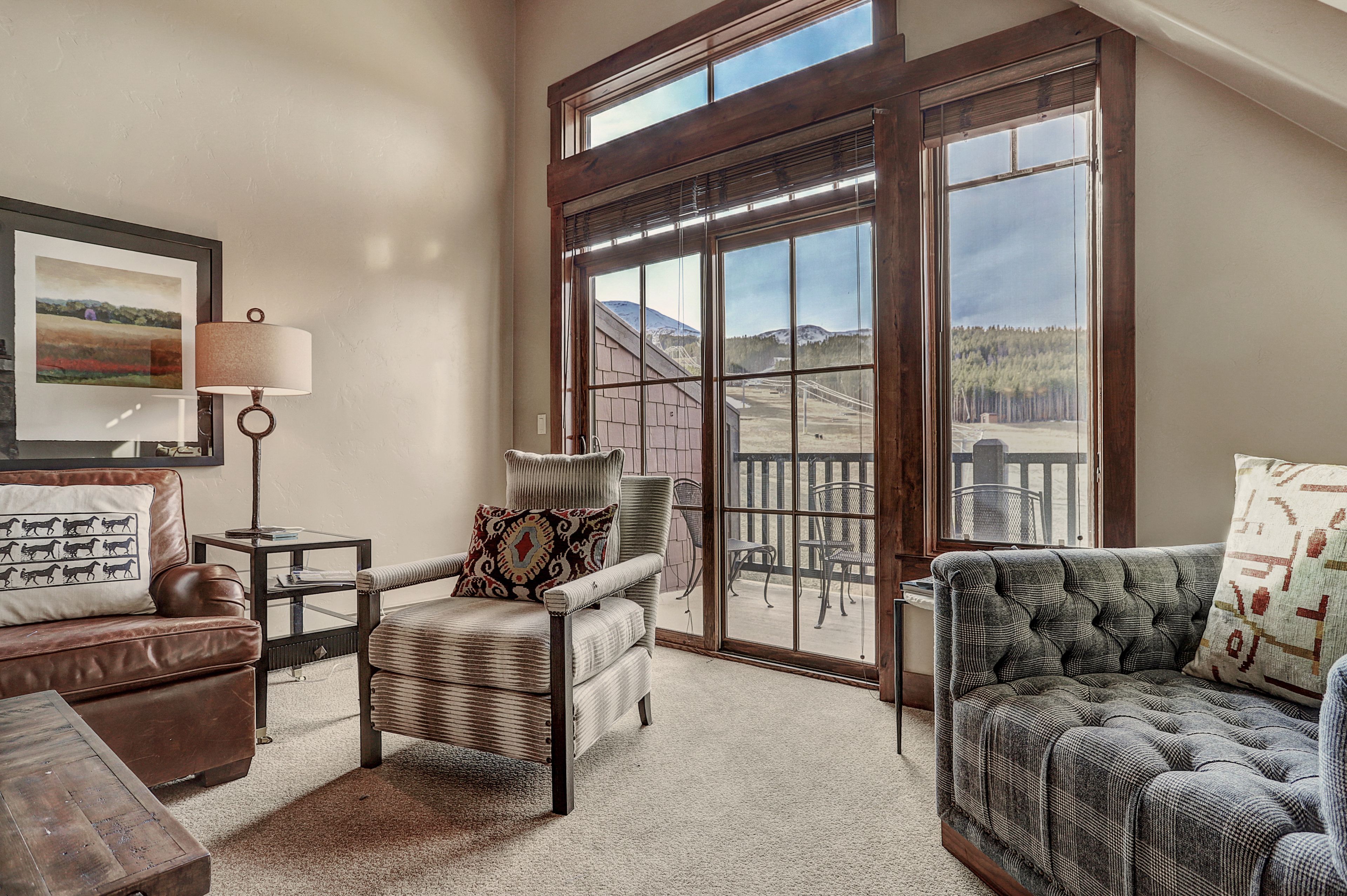 A cozy living room with a large window, a framed picture, and a lamp.