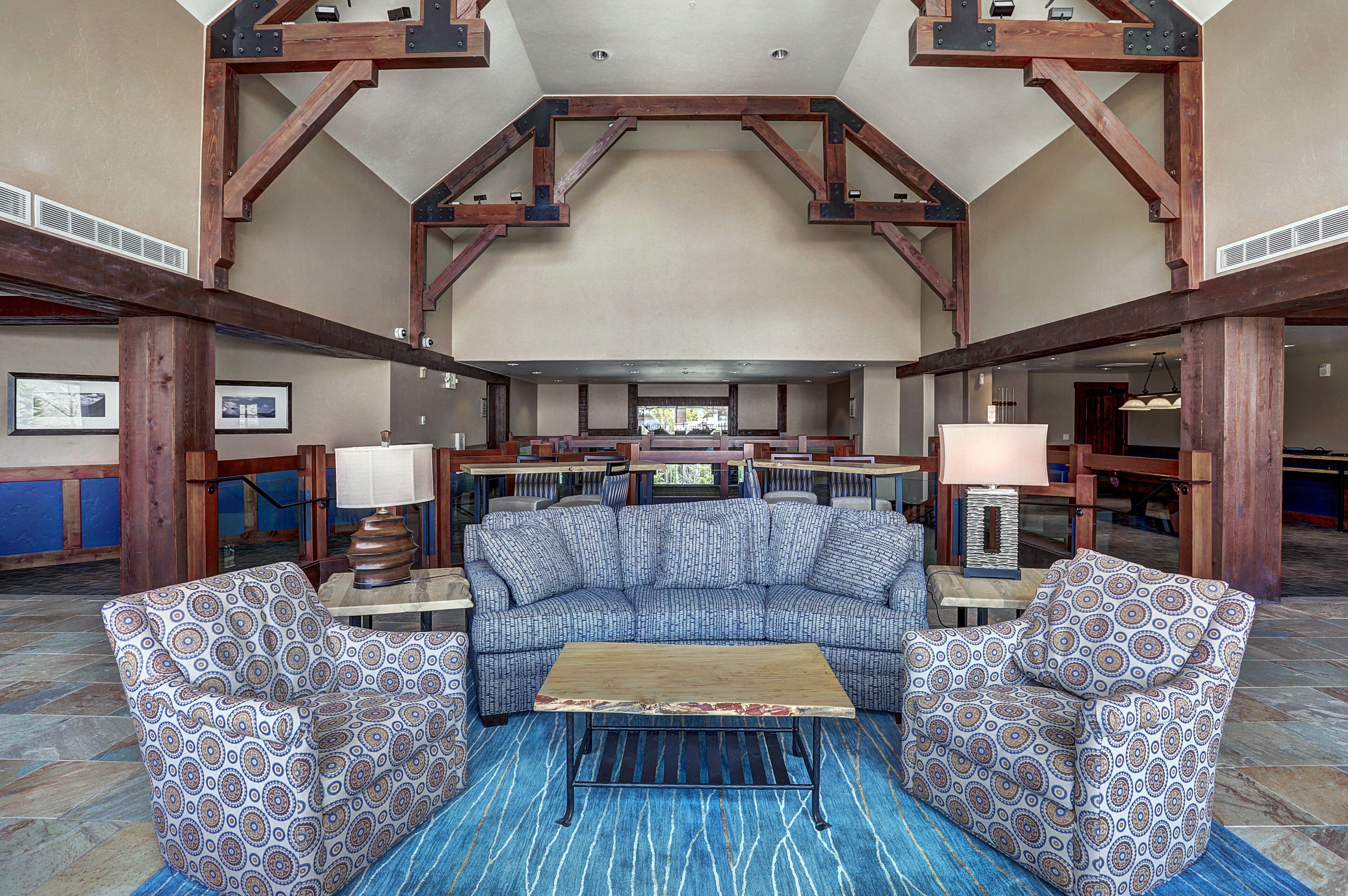 A spacious lobby with a large sectional sofa, two patterned armchairs, a wooden coffee table, and a blue patterned rug.