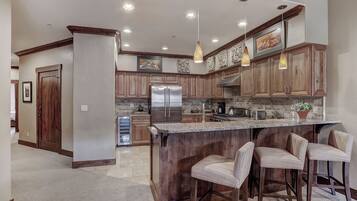 A kitchen with wooden cabinets, a stainless steel refrigerator, a granite countertop, and pendant lighting.