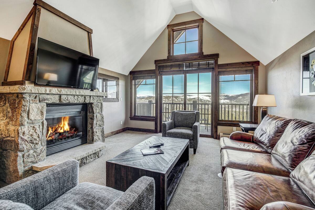 A cozy living room with a stone fireplace, comfortable seating, and a large window offering a scenic view.