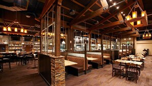 Un restaurante con vigas de madera, pilares de piedra y varias zonas de estar, incluyendo cabinas y mesas.