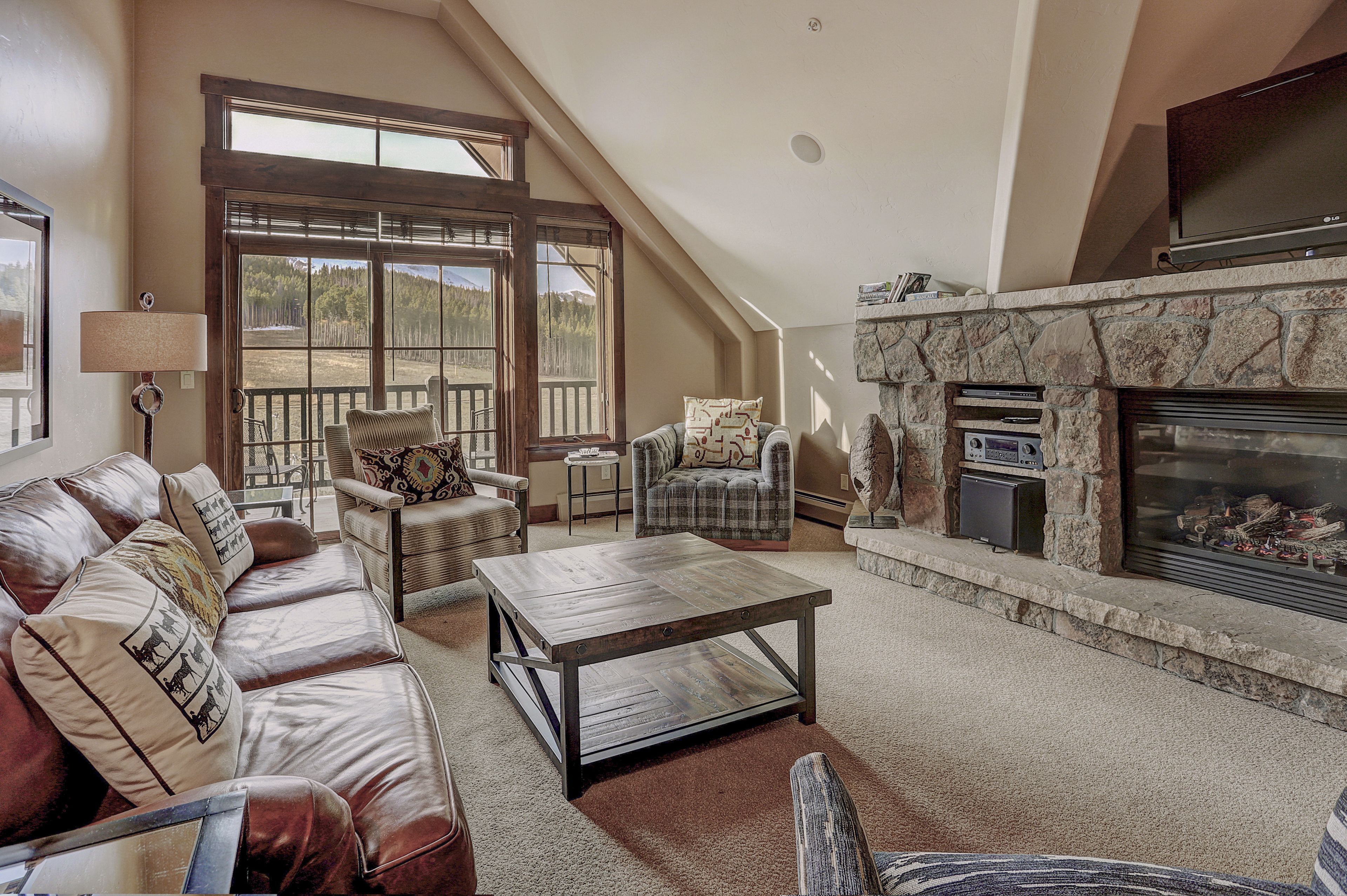 A spacious living room with a large window, a fireplace, leather sofas, and a coffee table.
