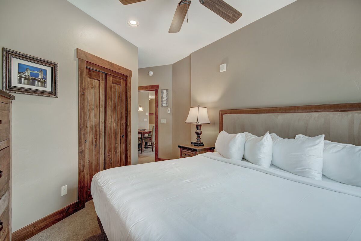 A bedroom with a large bed, wooden wardrobe, and a ceiling fan.