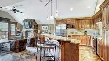 A spacious kitchen with wooden cabinets, a large island, and a stone fireplace.