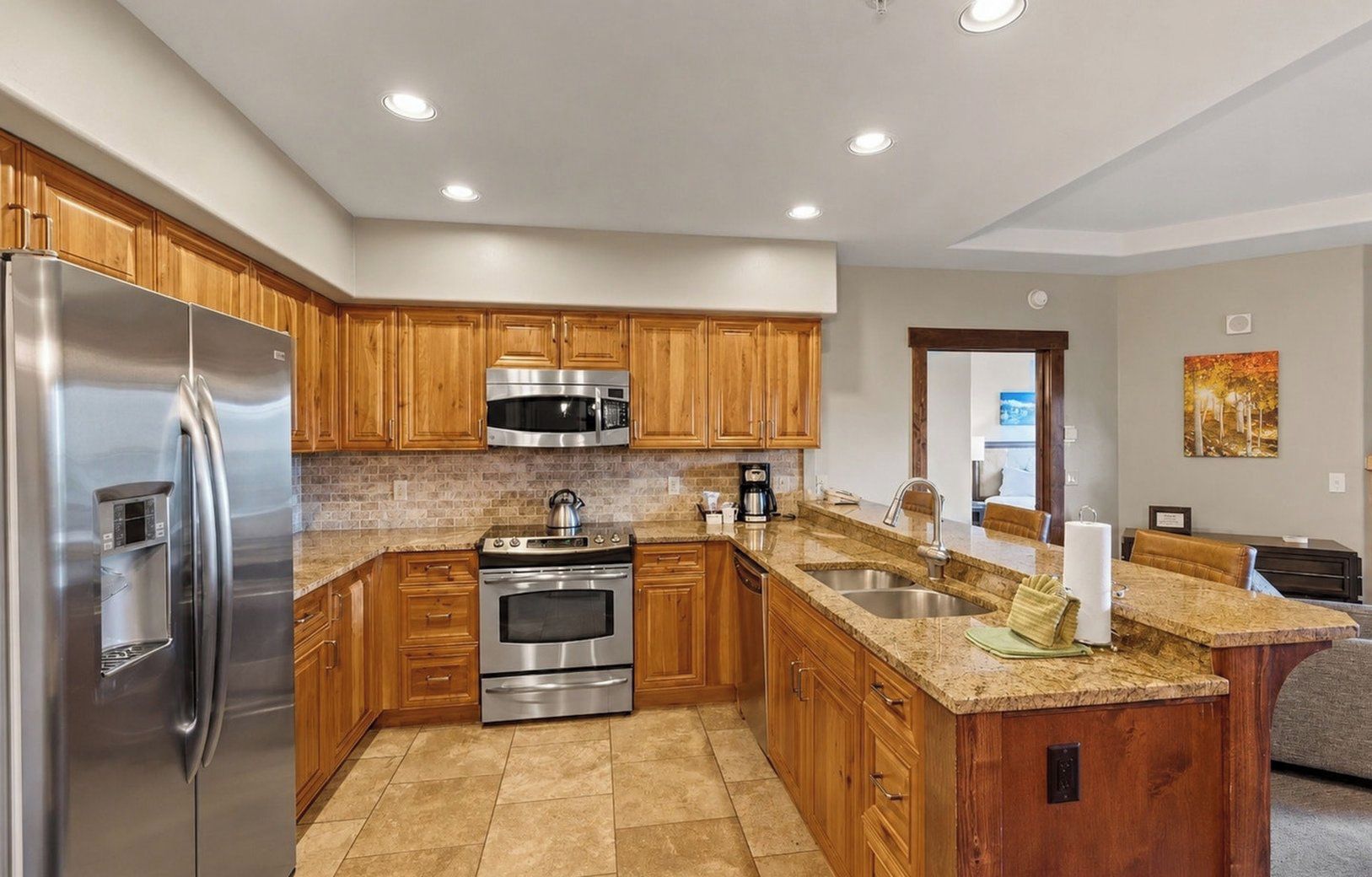 A modern kitchen with stainless steel appliances, wooden cabinets, granite countertops, and a built-in island with a sink.