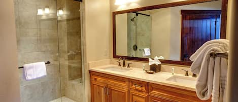 A bathroom with a glass-enclosed shower, wooden cabinets, a large mirror, and a towel rack.