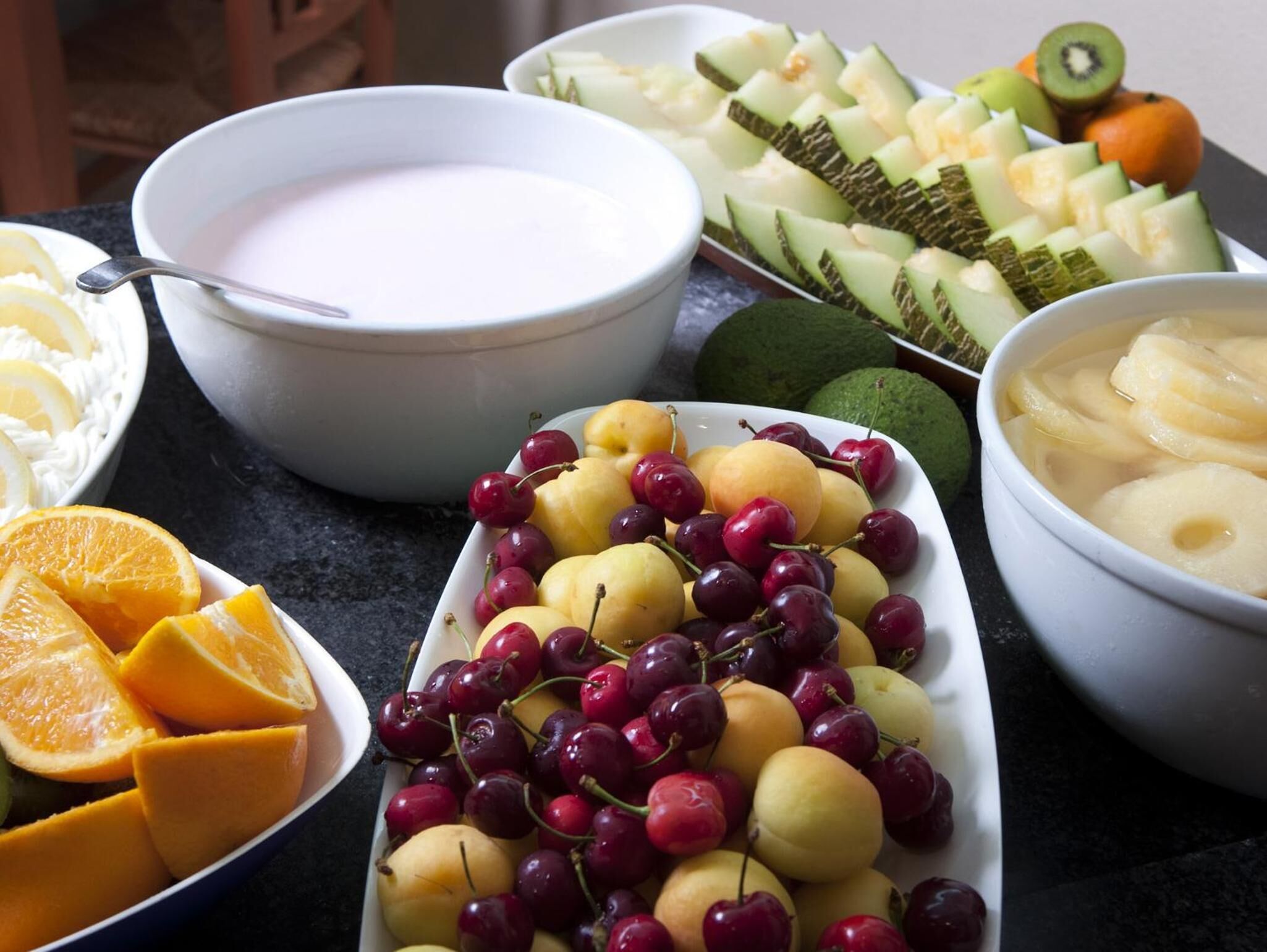 Una mesa con diversas frutas y un tazón de yogur.