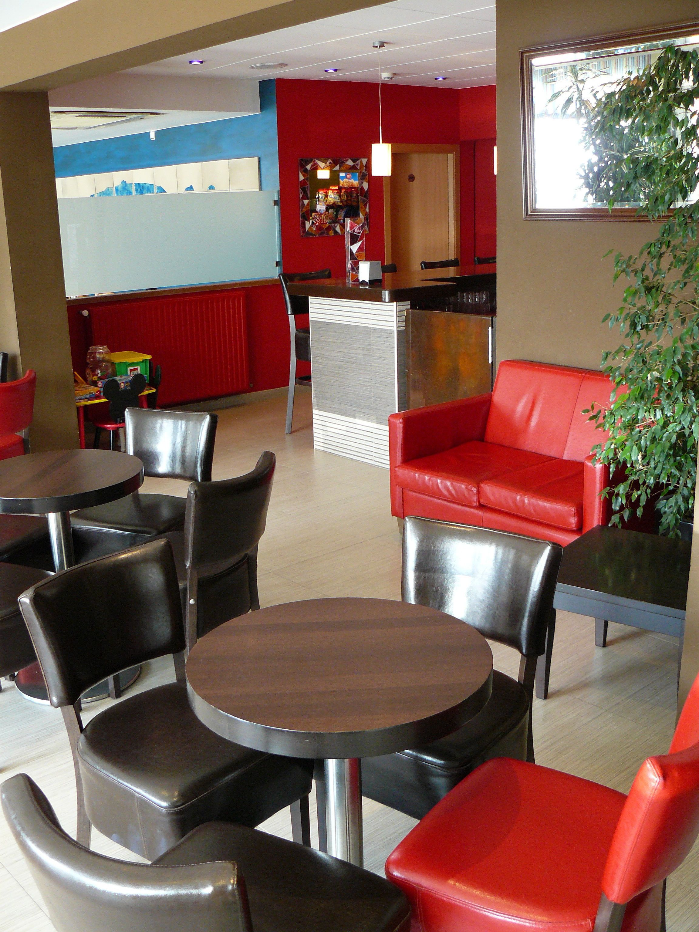 A restaurant interior with red and black chairs, a red sofa, and a counter.