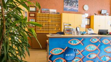 A hotel reception desk with a blue fish pattern, a clock, and a computer monitor on the wall.