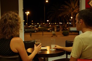Two people seated at a round table with a view of a parking lot and palm trees outside.