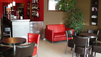 Un interior moderno con un sofá rojo, sillas negras, una pequeña mesa y una planta en maceta.