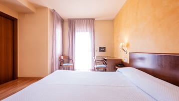 A hotel room with a large bed, a desk, two chairs, and a window with curtains.