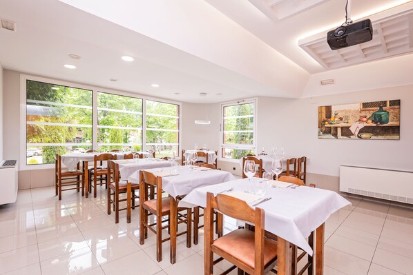 A dining area with multiple tables and chairs, large windows, and a ceiling projector. - Hotel La Perla (Olot)