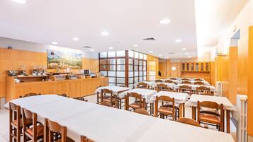 Un comedor amplio con varias mesas y sillas, una estación de buffet y un gran ventanal que proporciona luz natural.