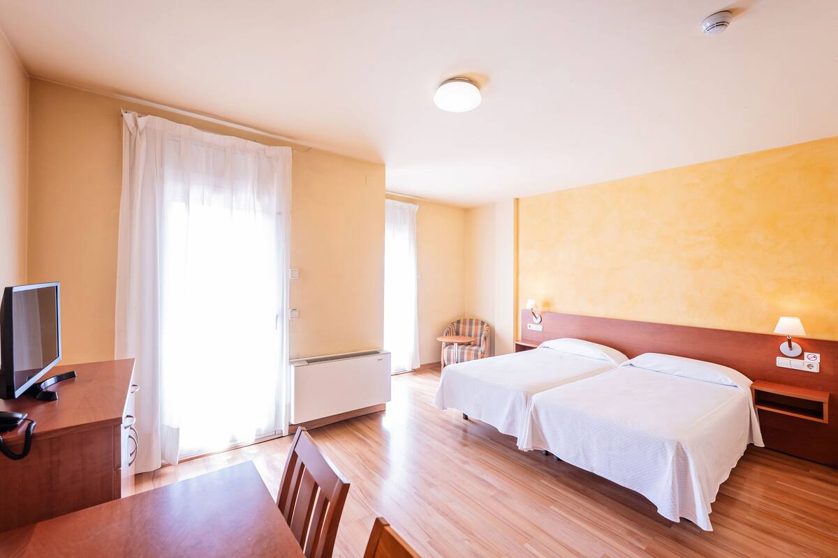 Habitación de hotel con dos camas, un escritorio con computadora y una silla.