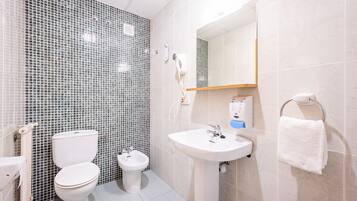 A bathroom with a toilet, bidet, and sink, tiled walls, and a towel rack.