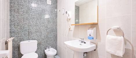 Baño con inodoro, bidé y lavamanos, paredes con azulejos y un perchero para toallas.