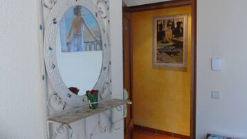 Un pasillo con un espejo decorativo, un cartel enmarcado y una pequeña estantería con un jarrón.