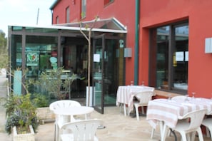 An outdoor seating area with white tables and chairs, a glass entrance, and a red building facade. - Restaurant Hotel Picasso (Torroella de Montgrí)