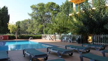 Una piscina con sillas de descanso y un patio amurallado con mesas y sillas.
