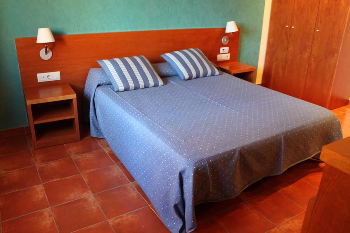 Ein Schlafzimmer mit einem hölzernen Kopfteil, zwei Nachttischen mit Lampen, einem Bett mit blauen Punkten-Bettwäsche und einem Holzschrank.