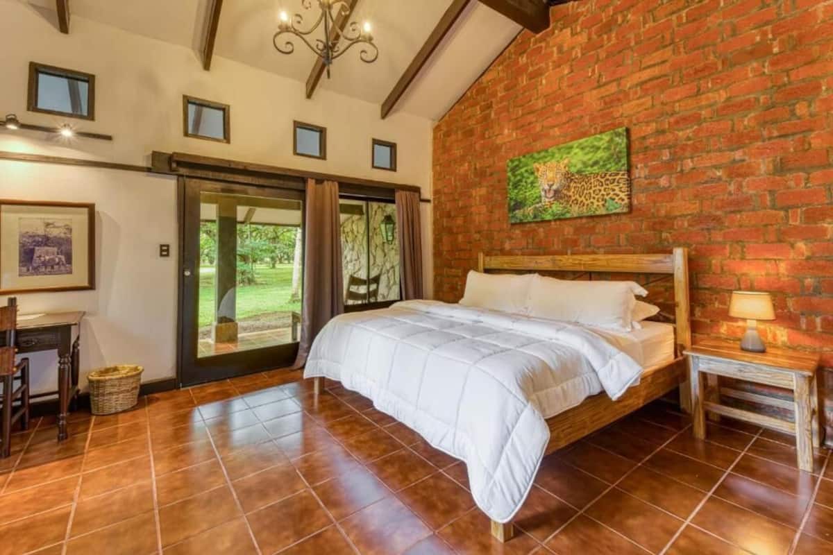 A bedroom with a large bed, a brick wall, a chandelier, and a door leading to a balcony.