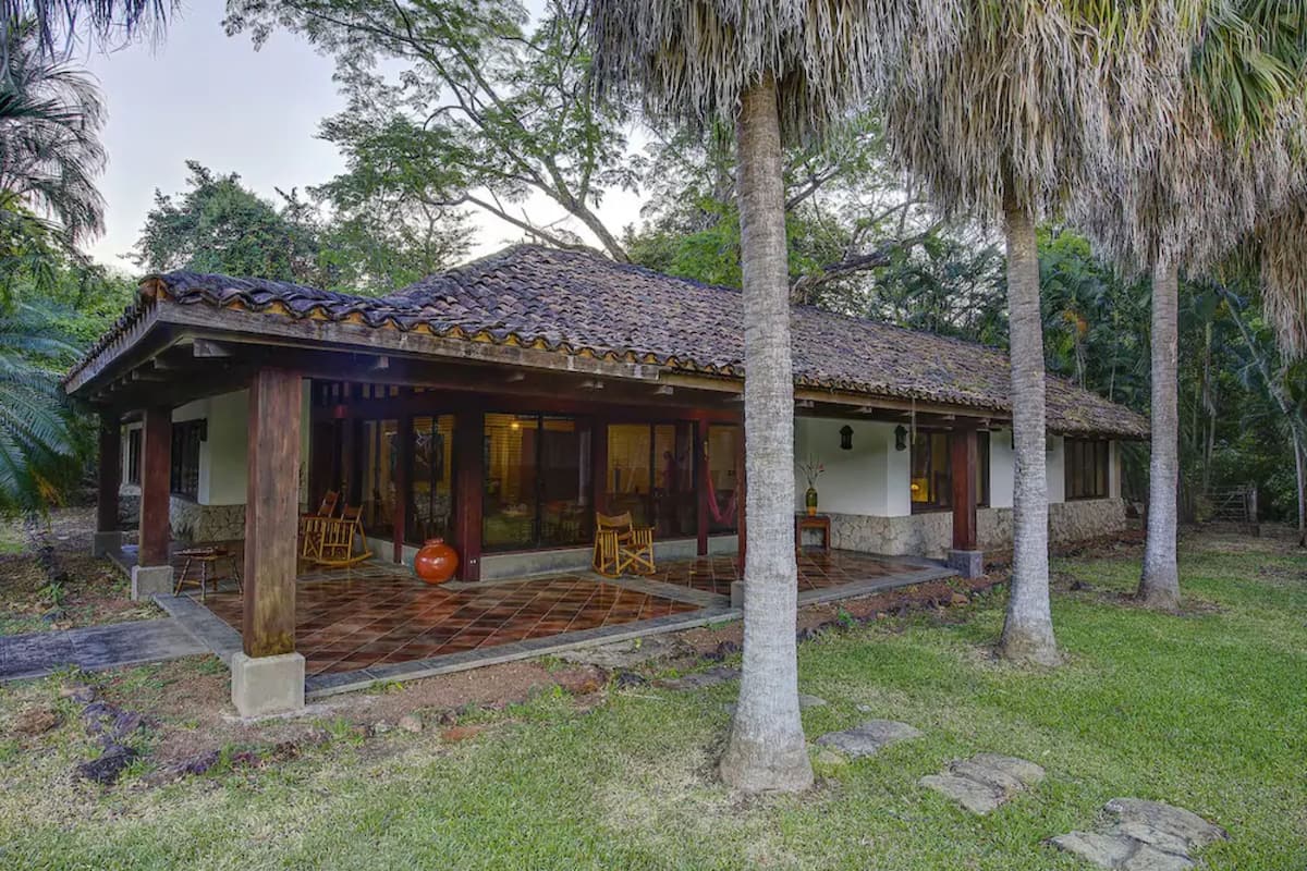 A house with a tiled roof, wooden pillars, and a porch with chairs.