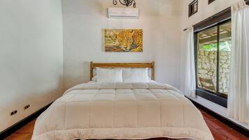 A bedroom with a wooden bed, white bedding, a leopard painting on the wall, and a stone wall visible through the window.