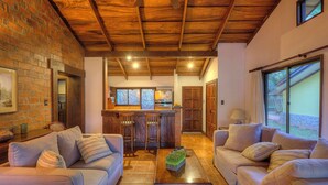 A spacious living area with a kitchen in the background, featuring wooden beams, brick walls, and large windows. - Hacienda La Pacífica Eco-Lodge (Cañas)