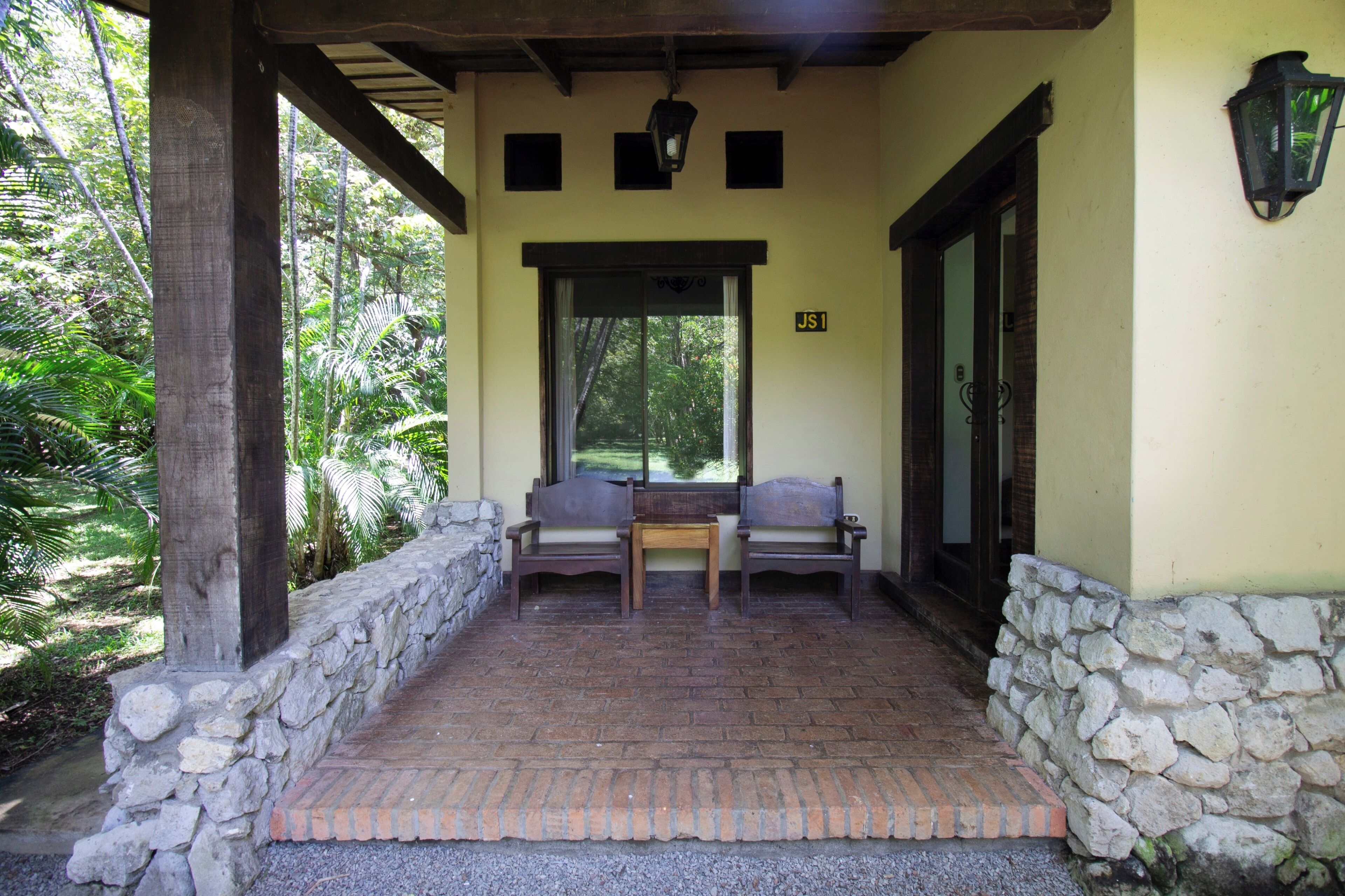 A covered outdoor seating area with stone walls, two wooden chairs, and a table.