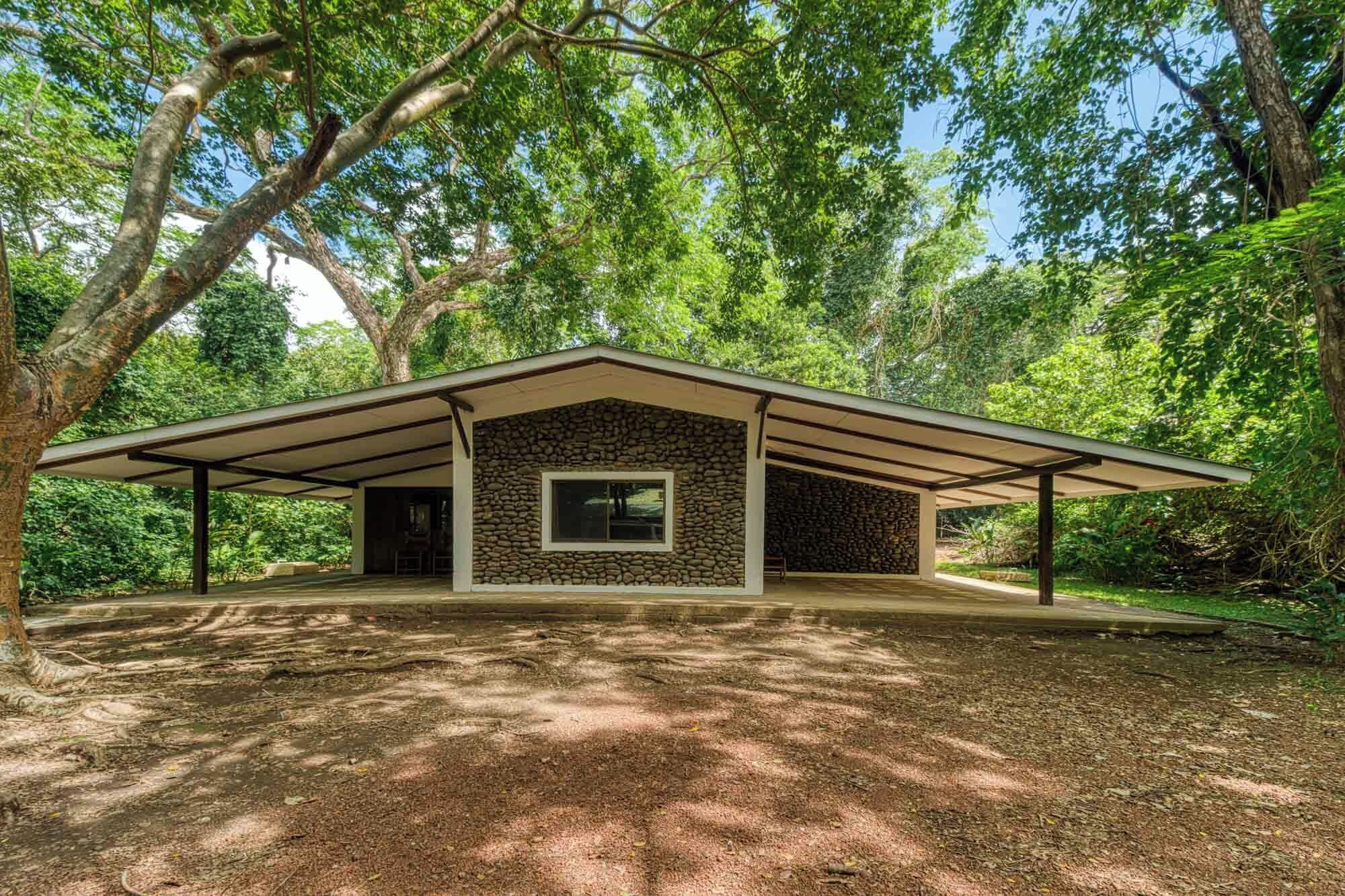 A single-story building with a stone facade and a flat roof, surrounded by dense trees.