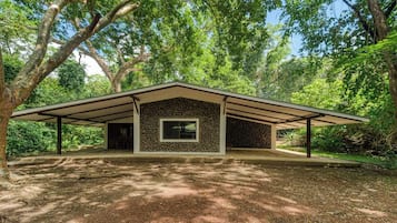 A single-story building with a stone facade and a flat roof, surrounded by dense trees.