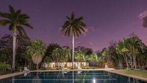A swimming pool with clear blue water, surrounded by palm trees and a building in the background. - Hacienda La Pacífica Eco-Lodge (Cañas)