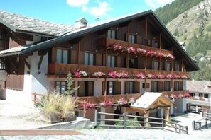 A multi-story wooden building with balconies adorned with flowers, set against a mountainous backdrop. - Hotel de Champoluc (Ayas)