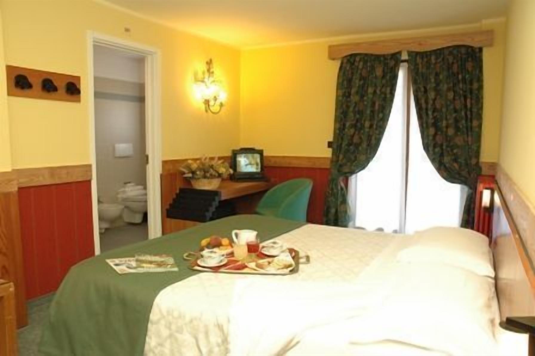 A hotel room with a bed, a desk with a chair, a television, and a window with curtains.