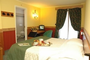 A hotel room with a bed, a desk with a chair, a television, and a window with curtains. - Hotel de Champoluc (Ayas)
