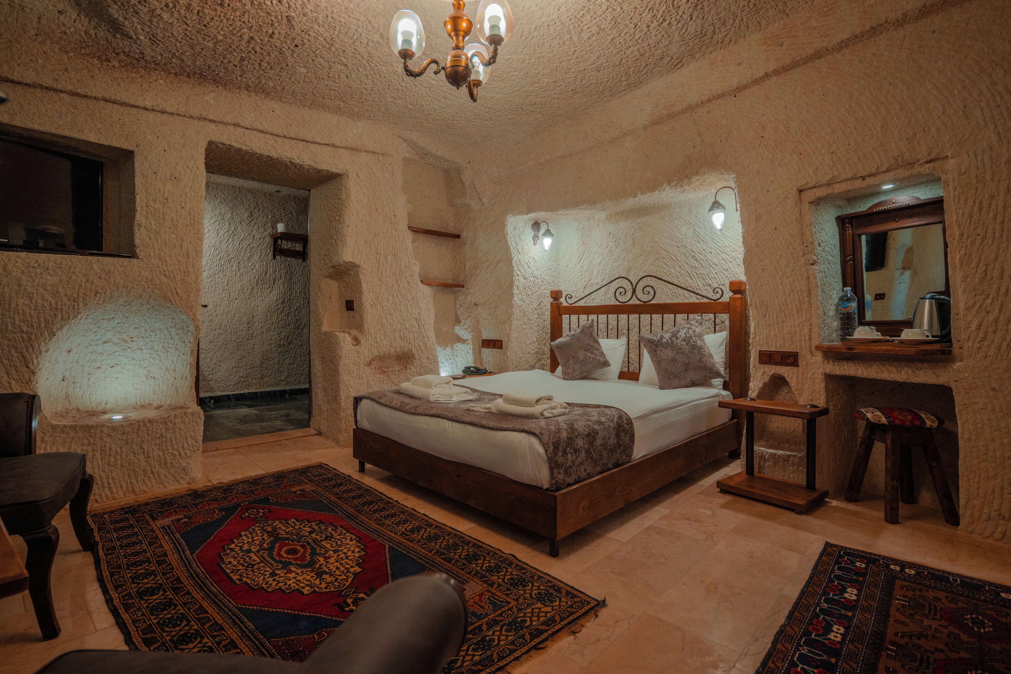 Un dormitorio con una cama grande, una mesita de noche de madera, una silla, una alfombra y un candelabro.