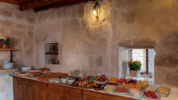 A rustic stone interior with a wooden ceiling, a buffet table with various foods, and a wall-mounted light fixture.