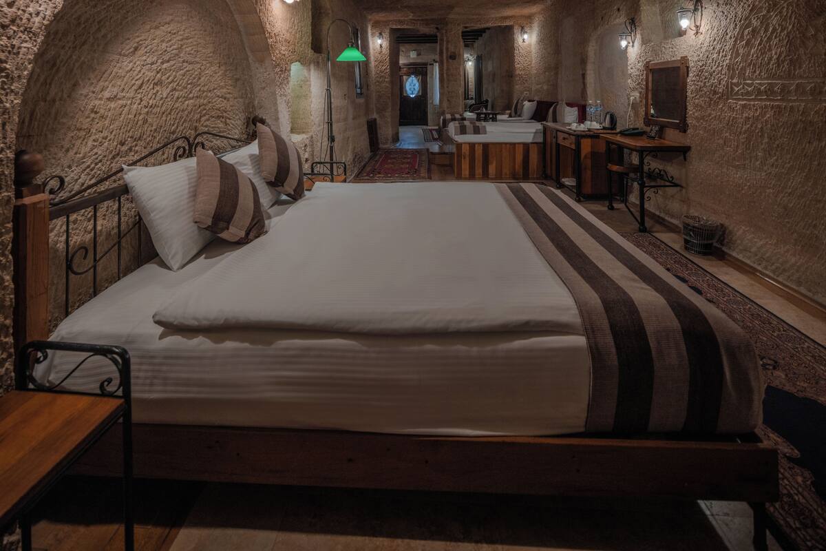 Un dormitorio con una cama grande, un escritorio y una silla. Hay un espejo en la pared y una lámpara en el escritorio.