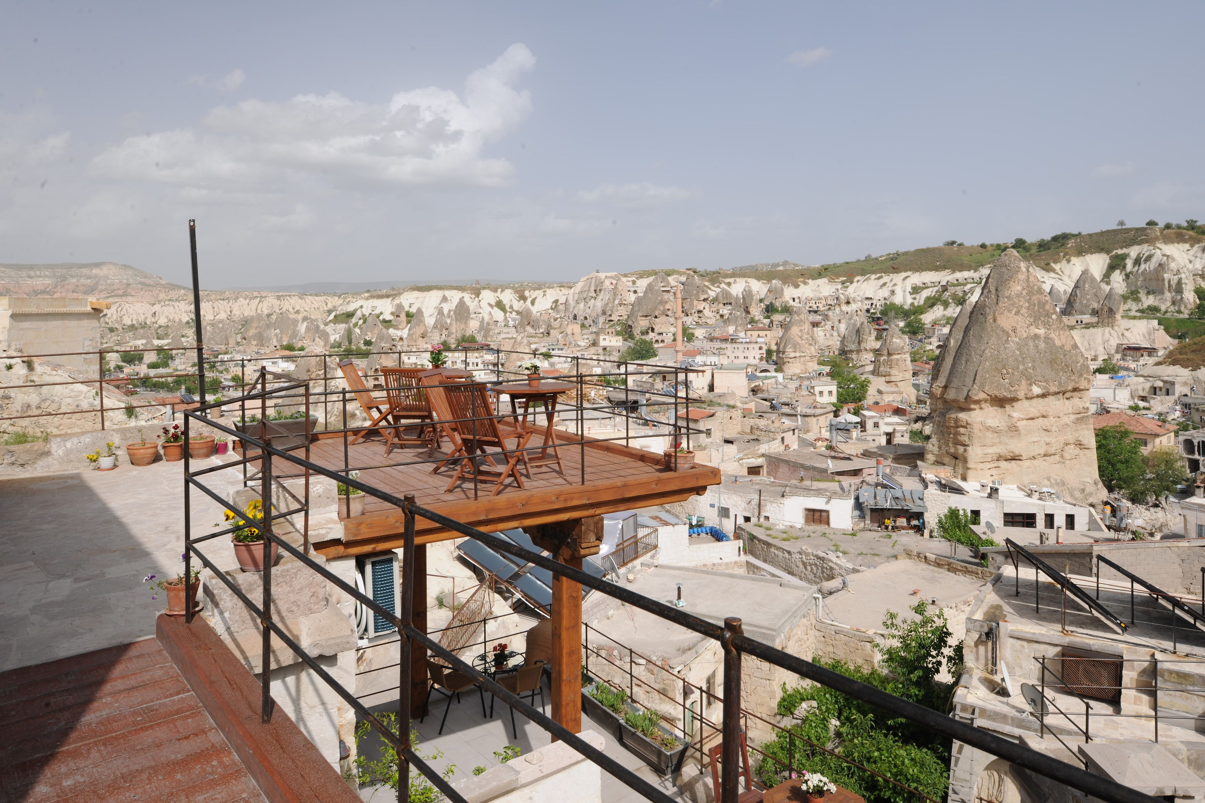 A rooftop terrace with a wooden table and chairs, overlooking a town with unique rock formations.