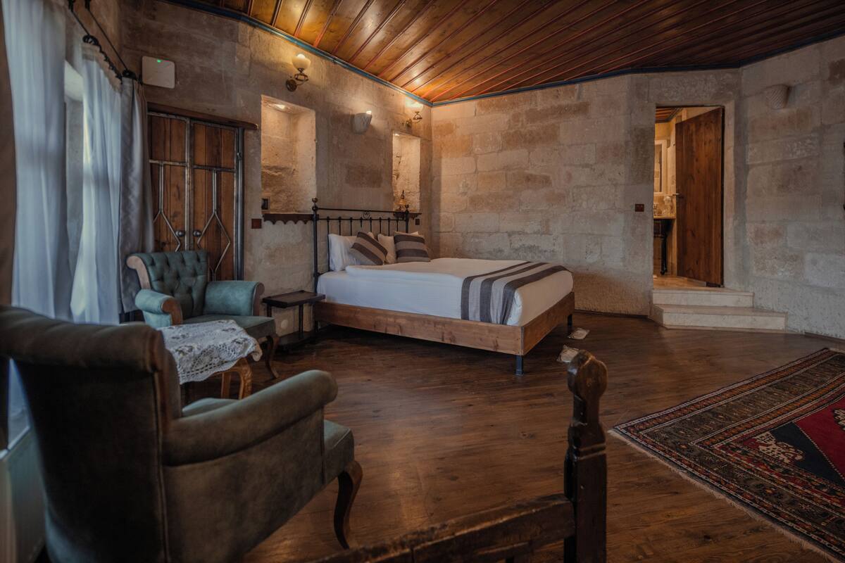 Un dormitorio rústico con cama de madera, un sillón antiguo y una pared de piedra.