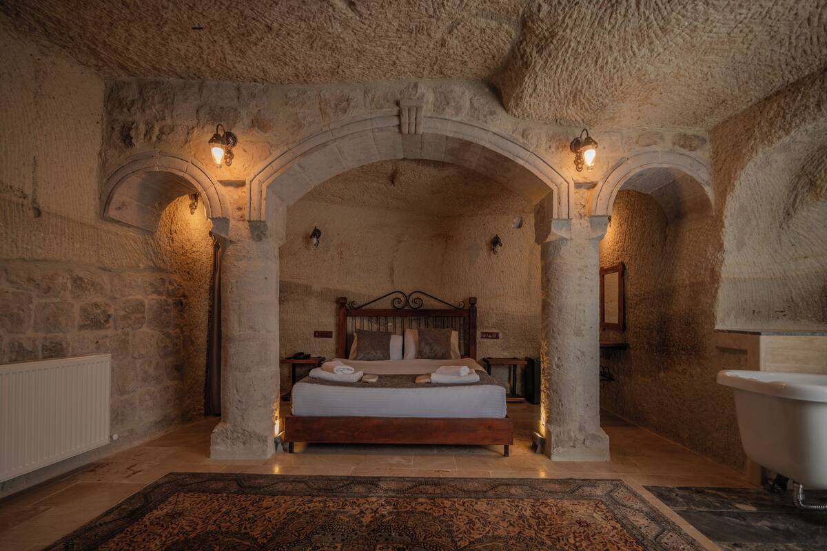 Un dormitorio con paredes de piedra, una cama de madera, dos mesitas de noche, un radiador blanco y una bañera.