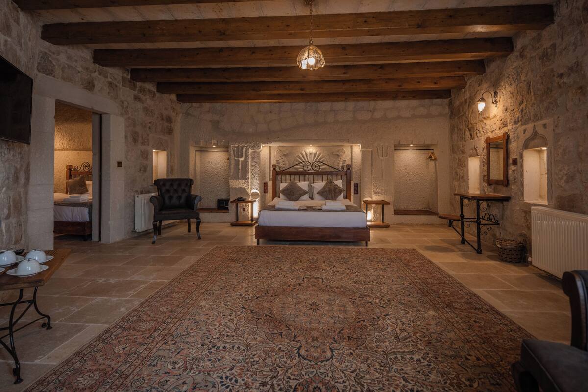 Un dormitorio espacioso con una cama grande, techo de madera, paredes de piedra y un tapiz estampado.