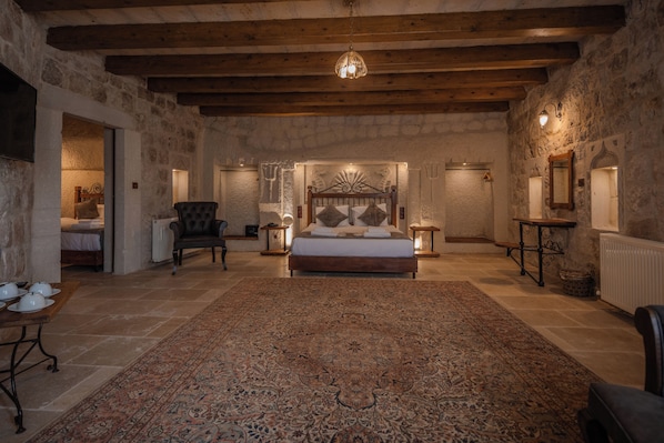 A spacious bedroom with a large bed, a wooden ceiling, stone walls, and a patterned rug.